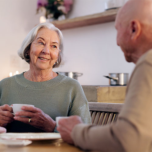 Seniorin lächelt beim Kaffeetrinken mit Betreuer – Symbol für soziale Betreuung und Lebensfreude im Alter